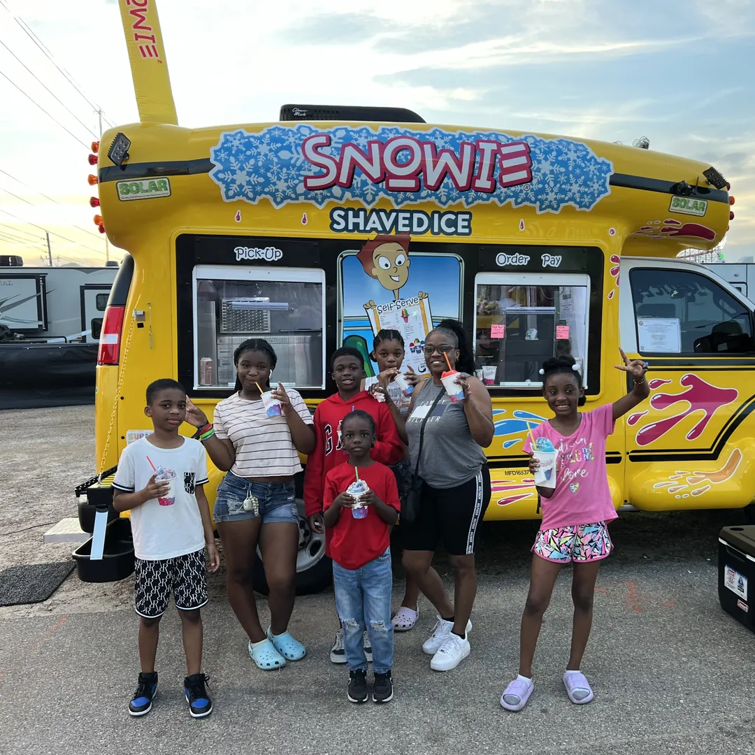 A family with their shaved ice in front of the bus at a fair