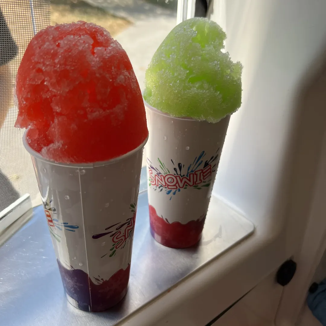 A red and a green Snowie Shaved Ice in tall Snowie cups