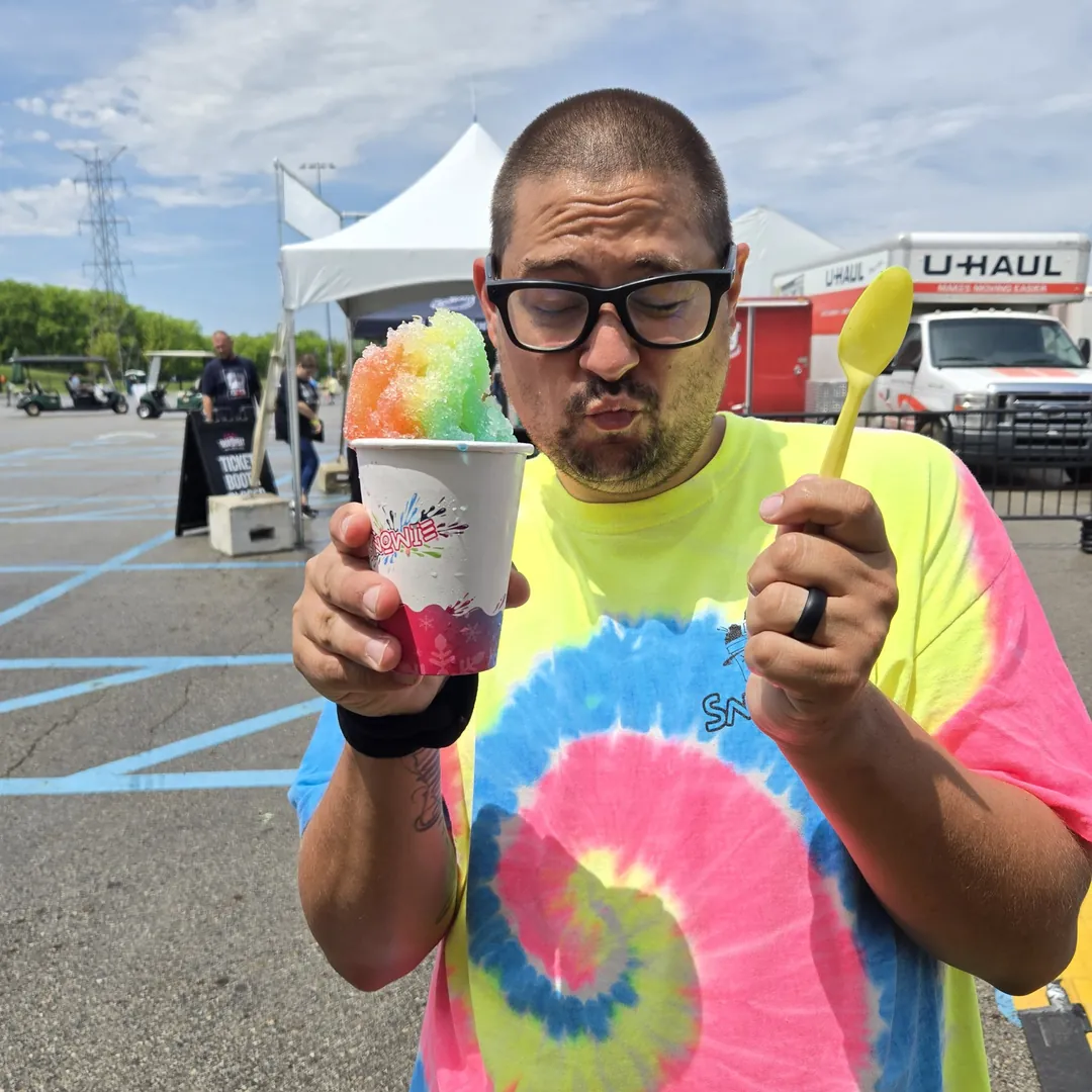A man in a tie-dye Snowie shirt about to dig into a rainbow shaved ice