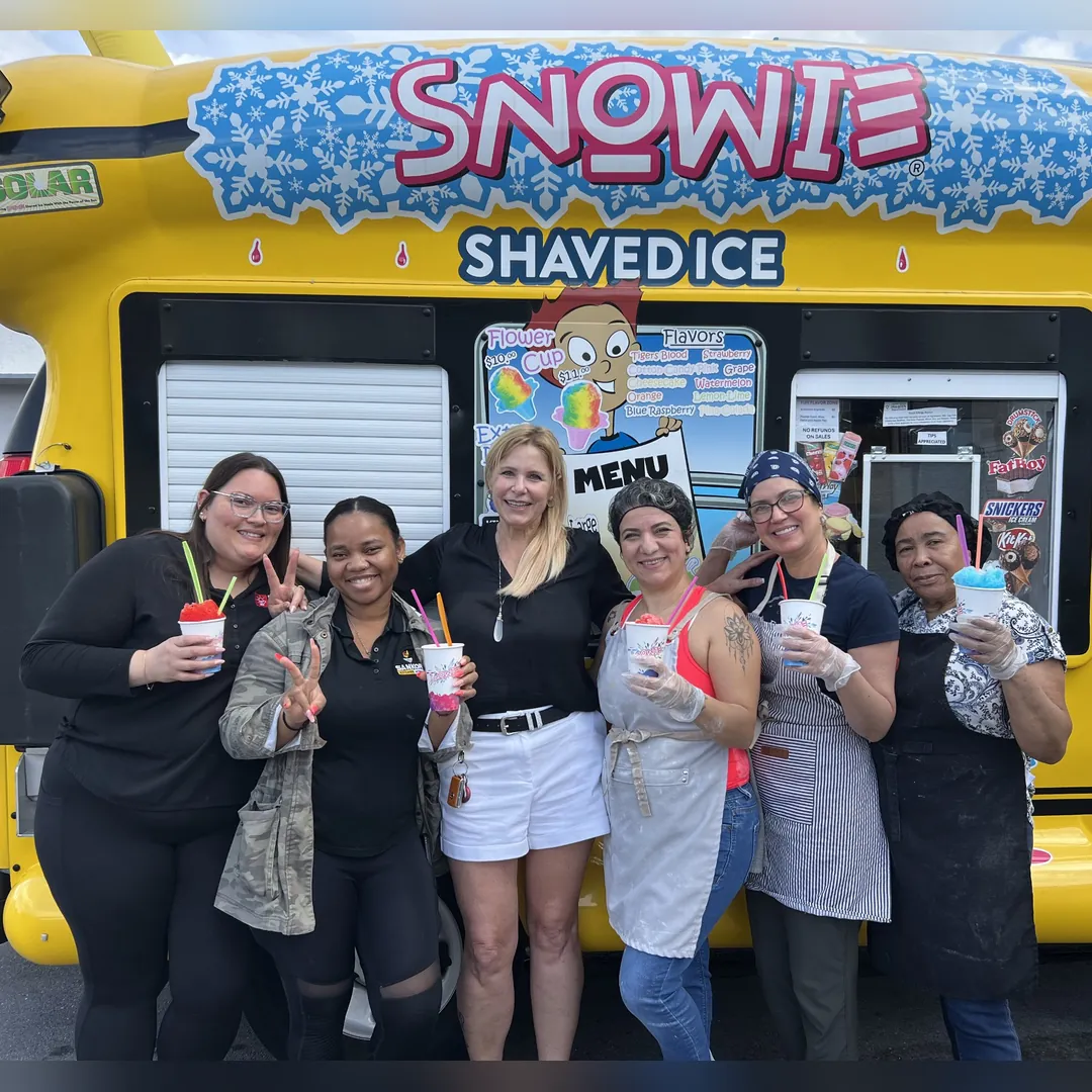 Six women holding shaved ice in front of the bus's menu window