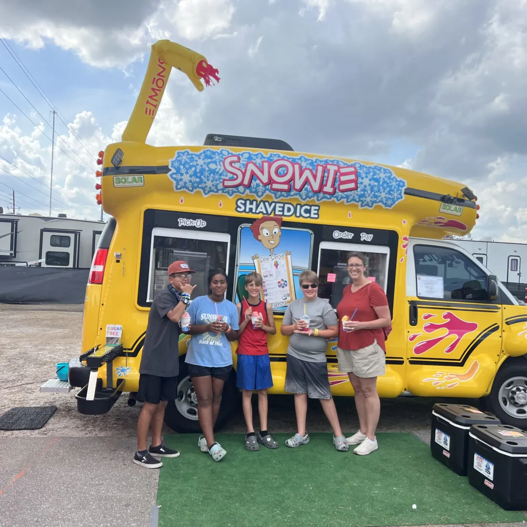 Four kids and a mom with shaved ice in front of the bus at a fair