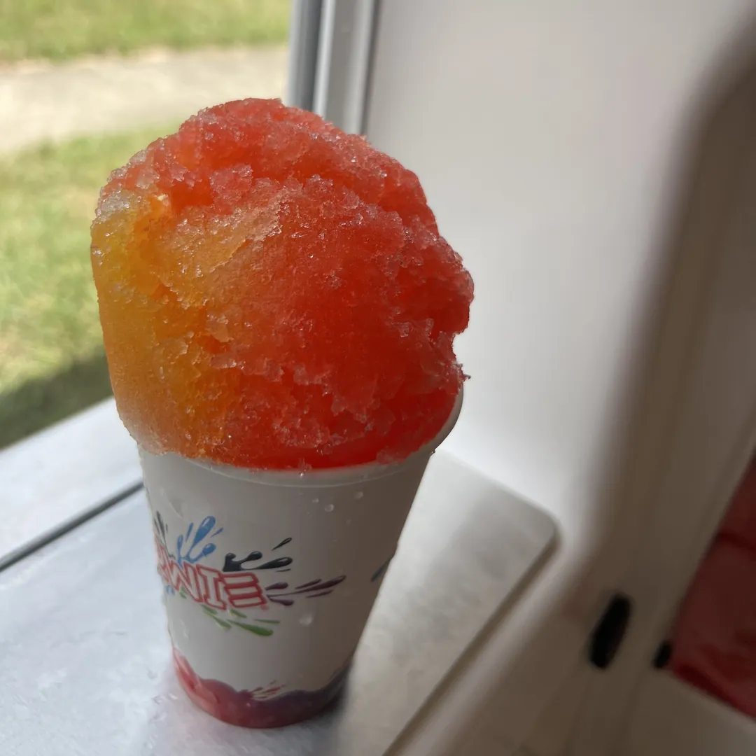 An orange and red Snowie Shaved Ice on the serving window ledge