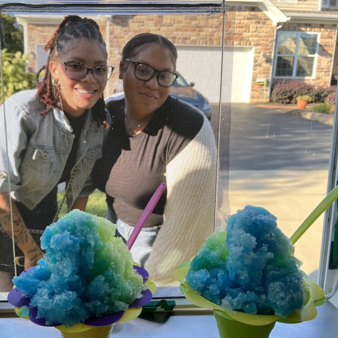 Two friends smiling through the serving window behind their blue and green Flower Cups