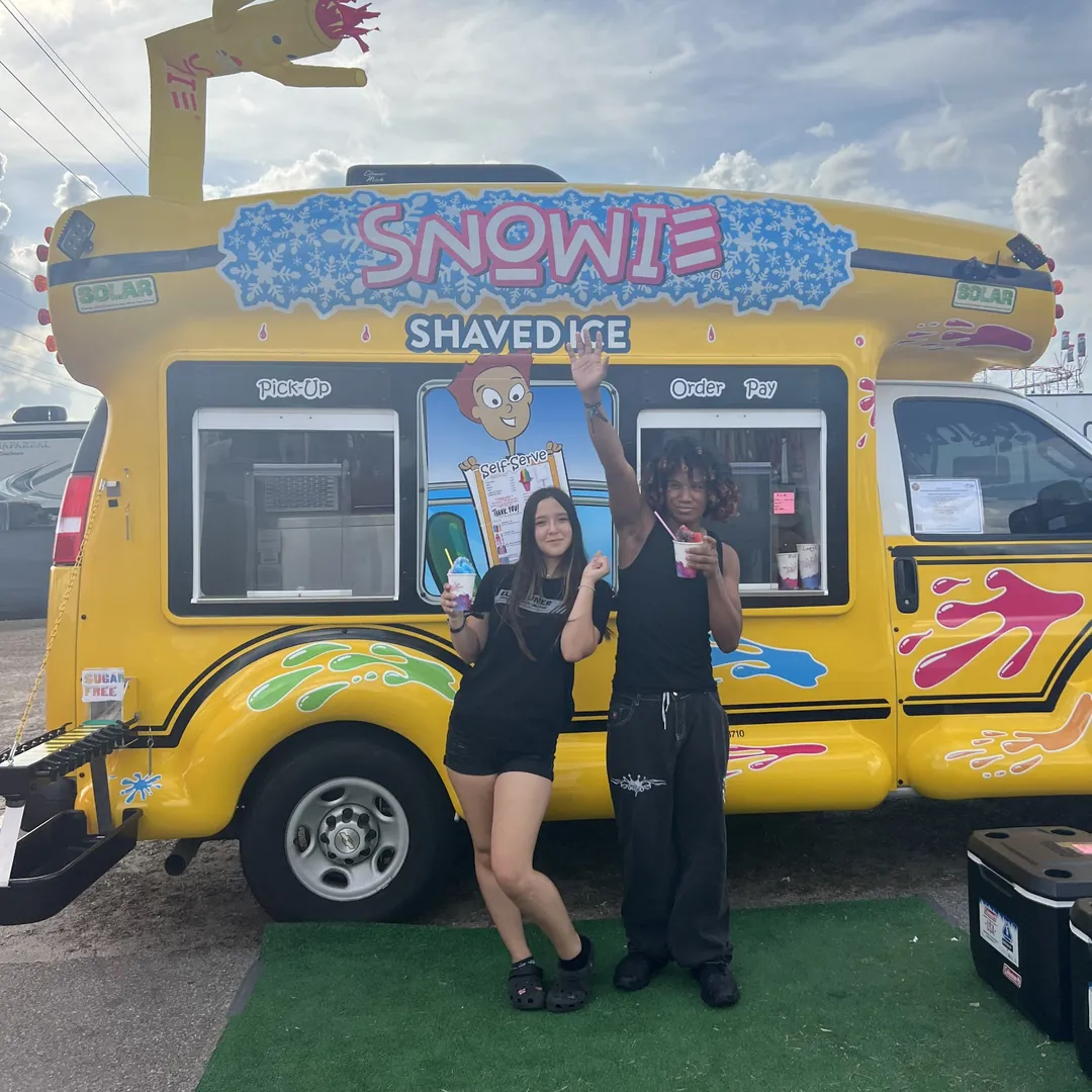 Two teens with shaved ice in front of the bus, one waving