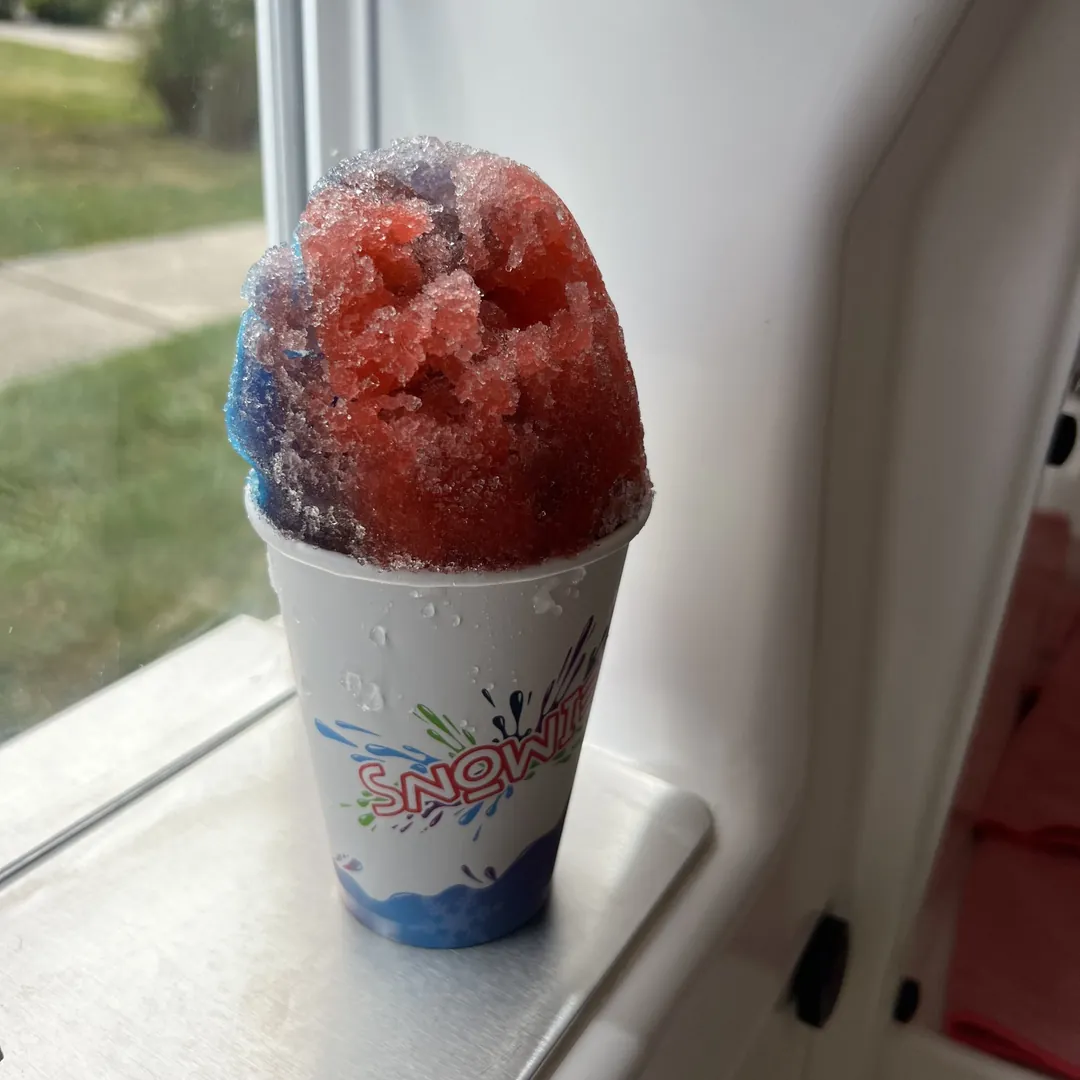 A red, purple and blue Snowie Shaved Ice on the serving window ledge