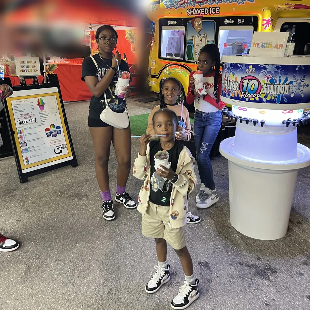 Kids enjoying shaved ice next to the Flavor Station at a fair at night