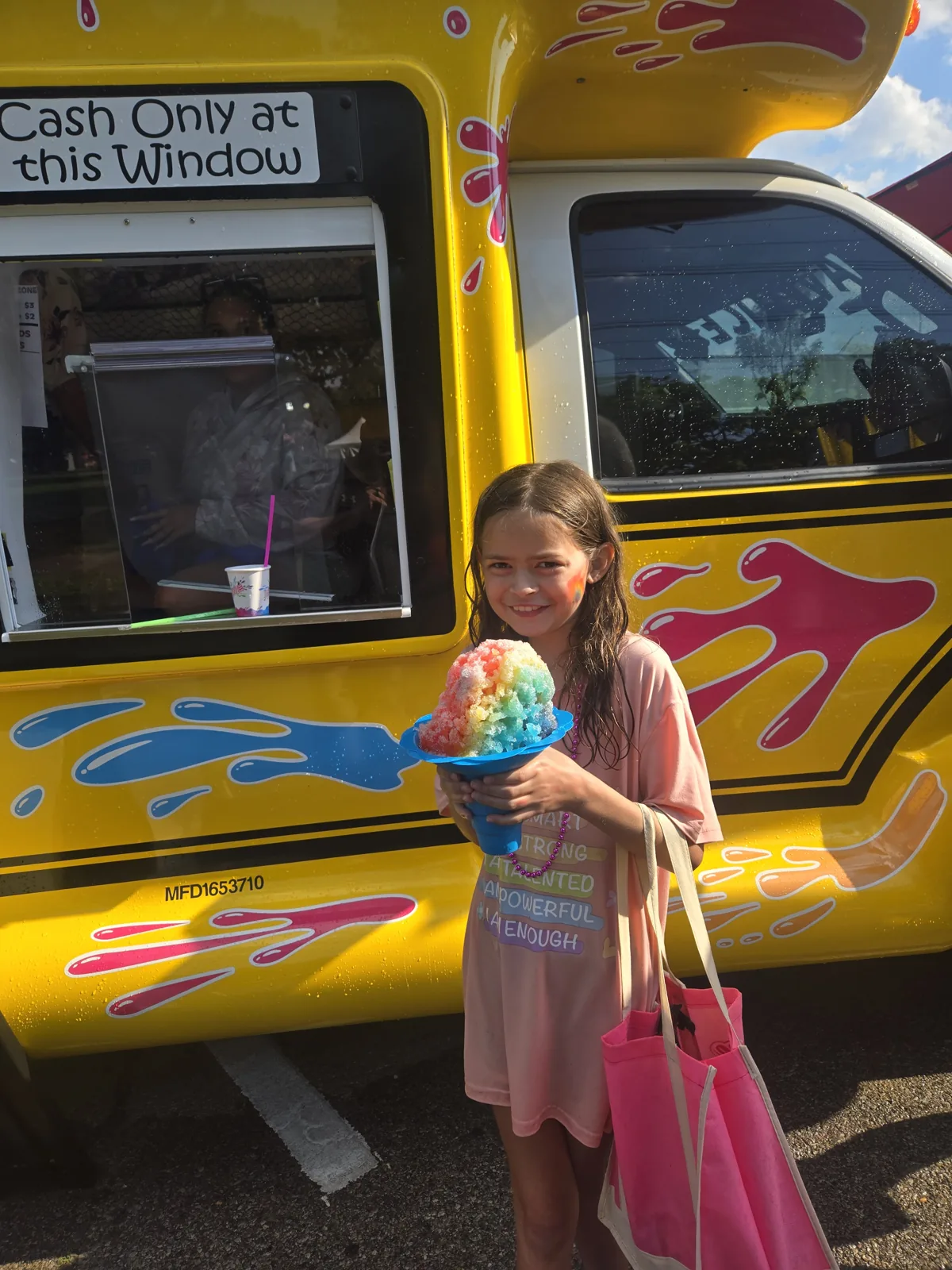 A girl holding a giant rainbow shaved ice in a Flower Cup next to the bus